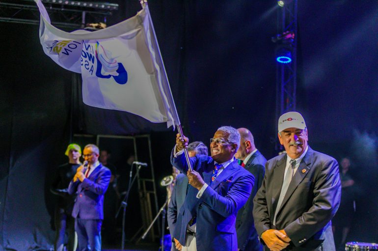 Photo of men on stage, one is waving a The World Games flag