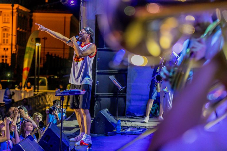 Photo of man interacting with crowd on stage surrounded by a brass band